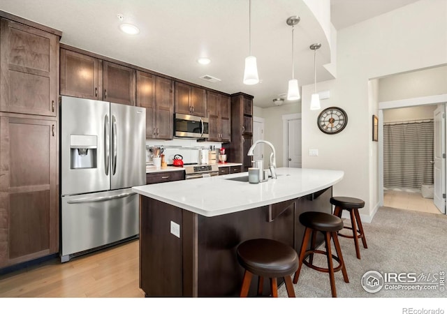 kitchen featuring appliances with stainless steel finishes, sink, dark brown cabinets, pendant lighting, and a center island with sink