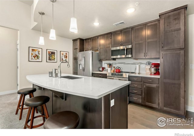 kitchen featuring pendant lighting, appliances with stainless steel finishes, sink, an island with sink, and dark brown cabinetry