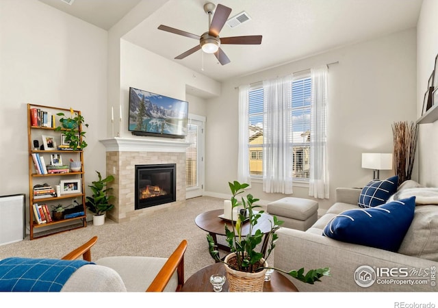 carpeted living room featuring ceiling fan and a tiled fireplace