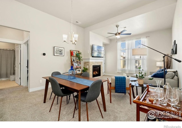 carpeted dining space with ceiling fan with notable chandelier and a tile fireplace