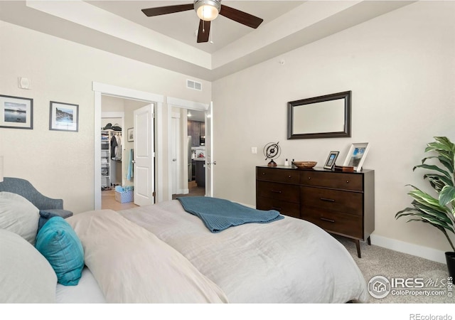 bedroom with a walk in closet, light carpet, a closet, ceiling fan, and a tray ceiling