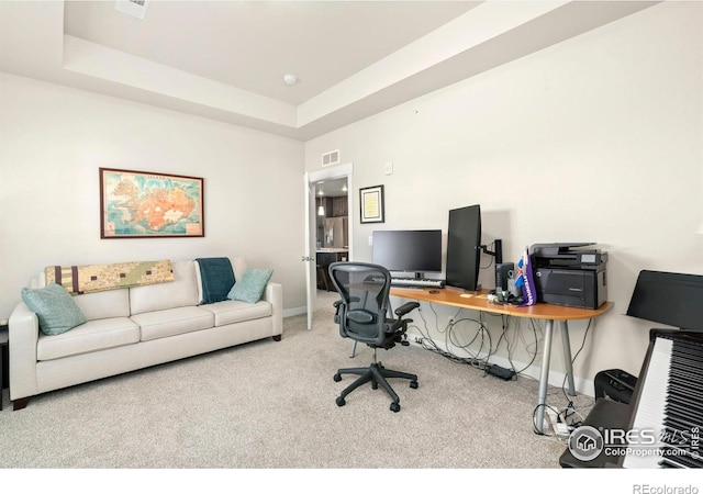 carpeted home office with a raised ceiling