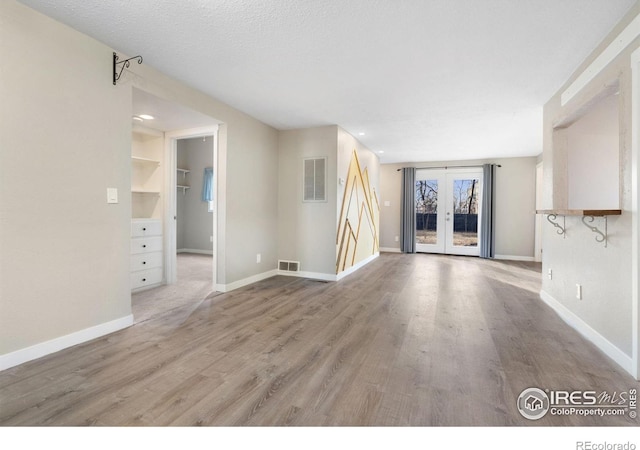 unfurnished living room featuring built in shelves, french doors, hardwood / wood-style floors, and a textured ceiling