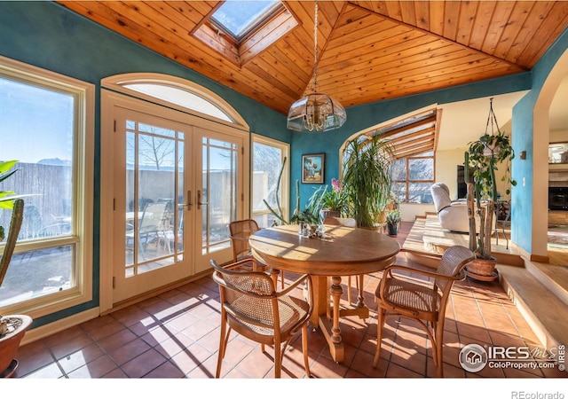 tiled dining area featuring french doors, vaulted ceiling with skylight, an inviting chandelier, and wood ceiling