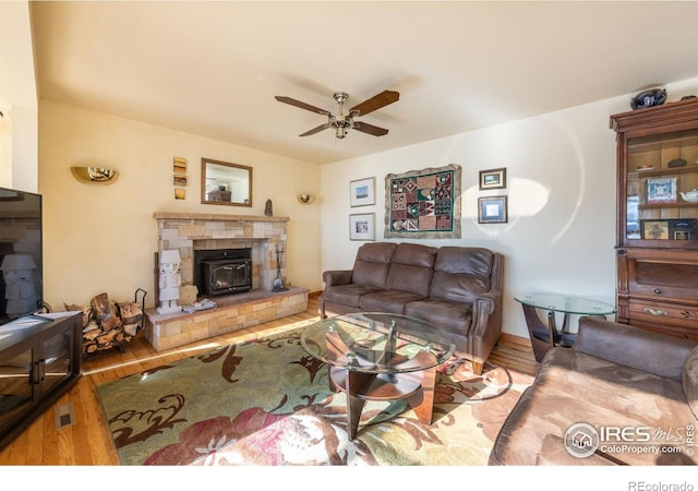 living room featuring ceiling fan, a wood stove, and light hardwood / wood-style flooring