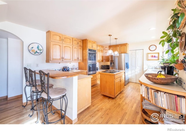 kitchen with a center island, stainless steel appliances, sink, hanging light fixtures, and light wood-type flooring