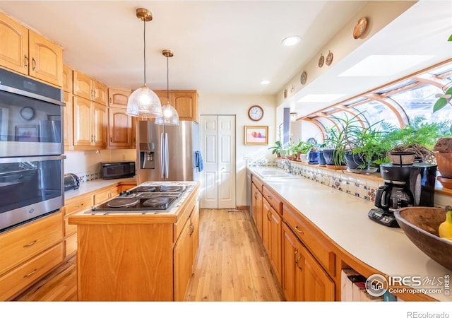 kitchen with a center island, light wood-type flooring, sink, pendant lighting, and stainless steel appliances