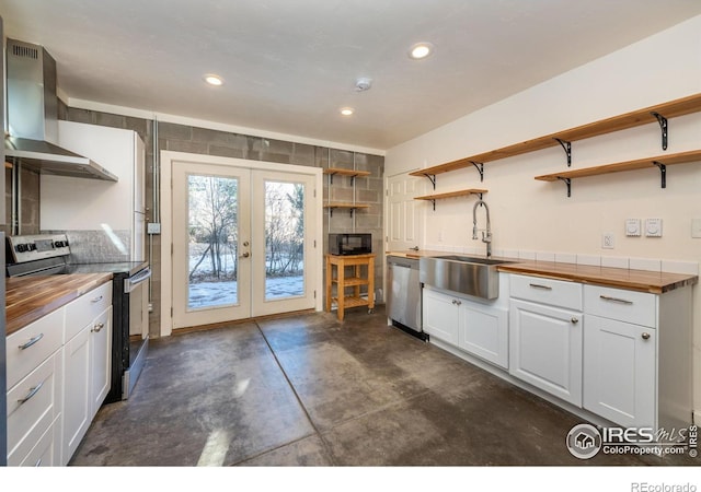 kitchen featuring white cabinets, appliances with stainless steel finishes, wall chimney range hood, sink, and butcher block countertops