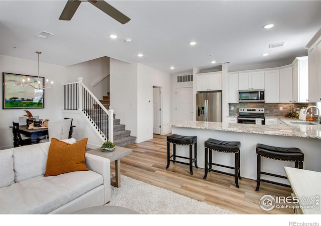 living room featuring light wood-type flooring, ceiling fan with notable chandelier, and sink