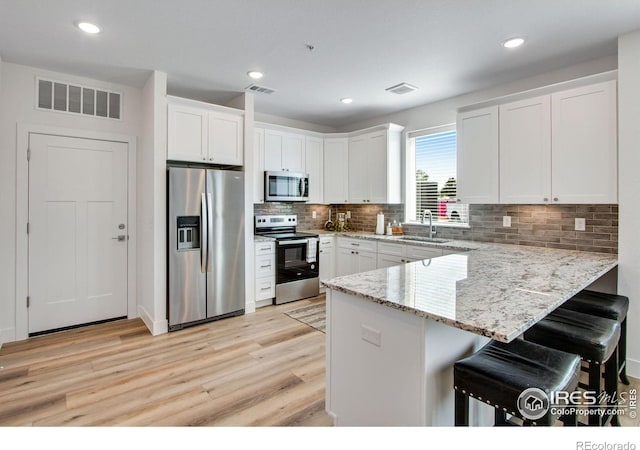 kitchen featuring white cabinets, stainless steel appliances, light stone countertops, and a kitchen breakfast bar