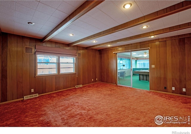 empty room with beamed ceiling, carpet, and wooden walls