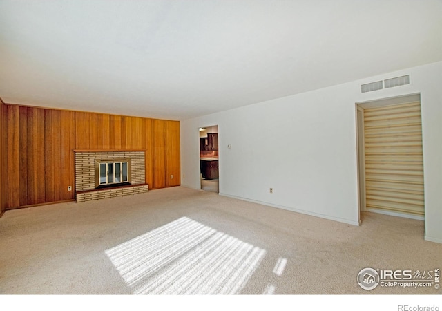 unfurnished living room featuring a fireplace, light colored carpet, and wooden walls