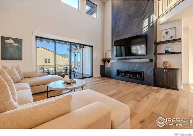 living room with light wood-type flooring, a high ceiling, and a tiled fireplace