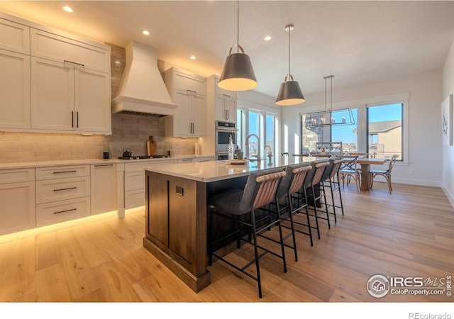 kitchen with white cabinetry, custom range hood, and an island with sink