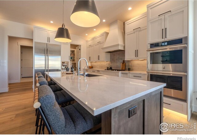 kitchen featuring sink, white cabinets, appliances with stainless steel finishes, and premium range hood