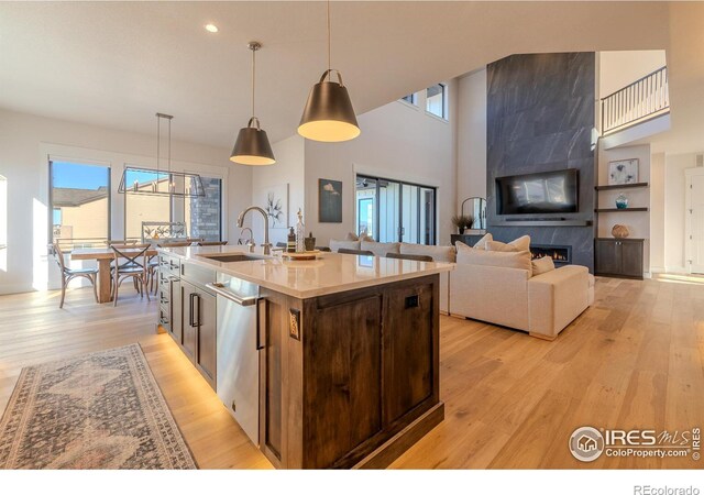 kitchen with dishwasher, decorative light fixtures, a fireplace, an island with sink, and sink