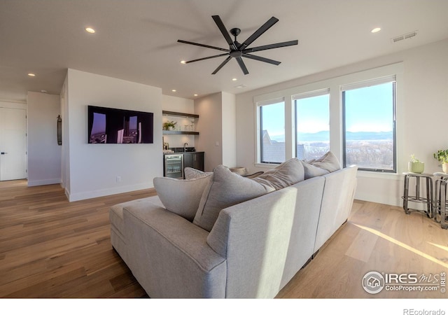 living room featuring ceiling fan, bar area, and light wood-type flooring