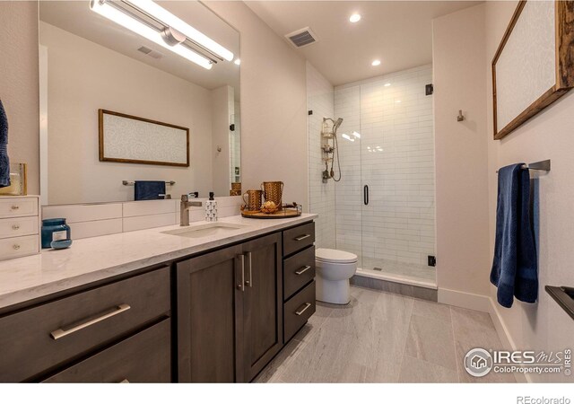 bathroom featuring a shower with door, toilet, and vanity