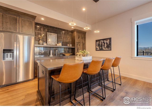 bar featuring decorative light fixtures, dark brown cabinets, light wood-type flooring, and stainless steel fridge