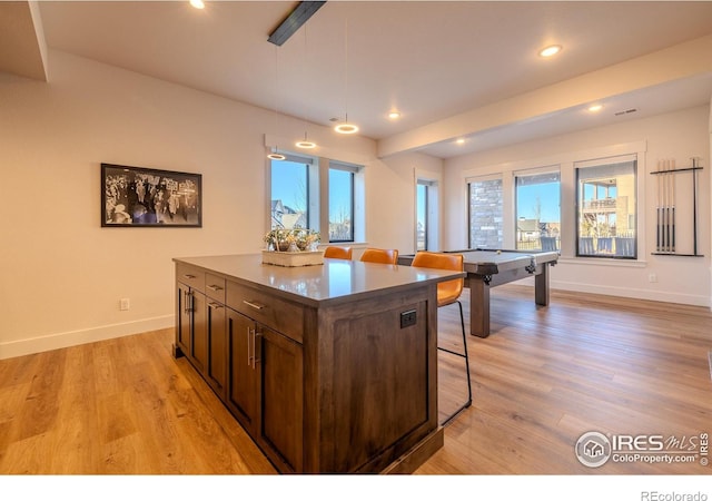 kitchen with a center island, light wood-type flooring, dark brown cabinetry, pendant lighting, and a breakfast bar