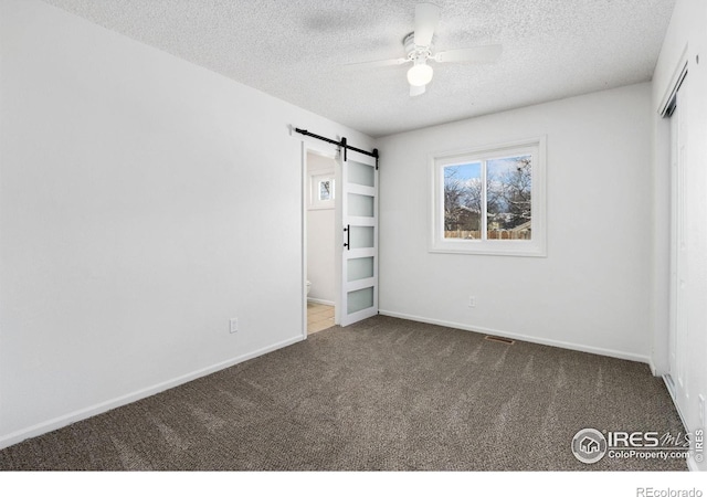 unfurnished bedroom featuring ceiling fan, a barn door, dark colored carpet, and a textured ceiling