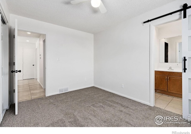 unfurnished bedroom with ceiling fan, a barn door, light colored carpet, and ensuite bath