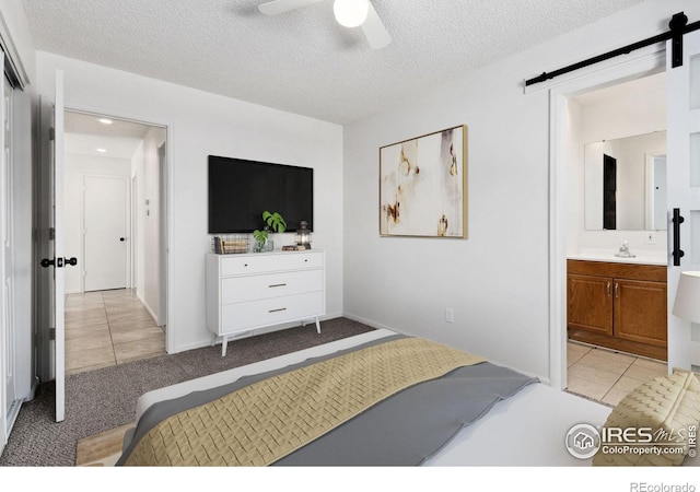 bedroom featuring a textured ceiling, ensuite bath, a barn door, ceiling fan, and light tile patterned flooring