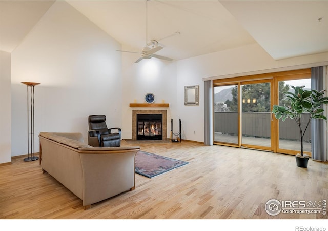 living room featuring a tile fireplace, lofted ceiling, ceiling fan, and light wood-type flooring