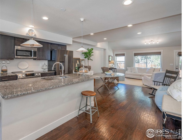 kitchen with light stone countertops, appliances with stainless steel finishes, dark hardwood / wood-style flooring, sink, and hanging light fixtures