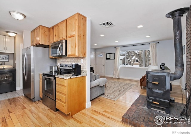 kitchen with appliances with stainless steel finishes, washer / dryer, light hardwood / wood-style floors, a wood stove, and backsplash