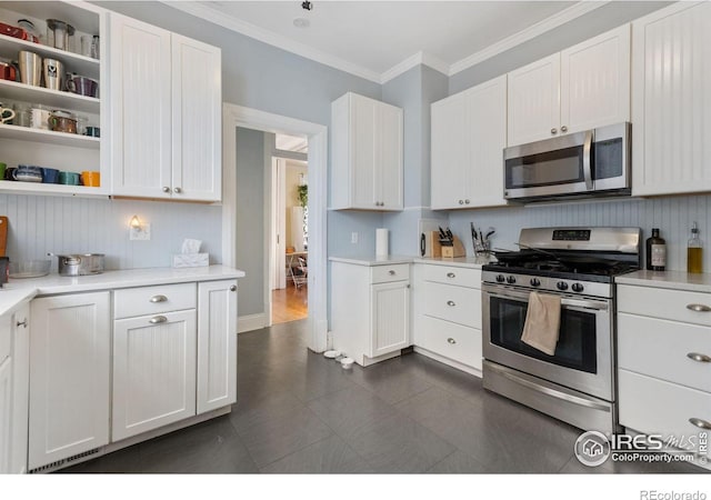 kitchen featuring white cabinets, appliances with stainless steel finishes, ornamental molding, and dark tile patterned floors