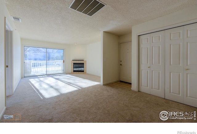 unfurnished living room featuring light colored carpet, a tile fireplace, and a textured ceiling