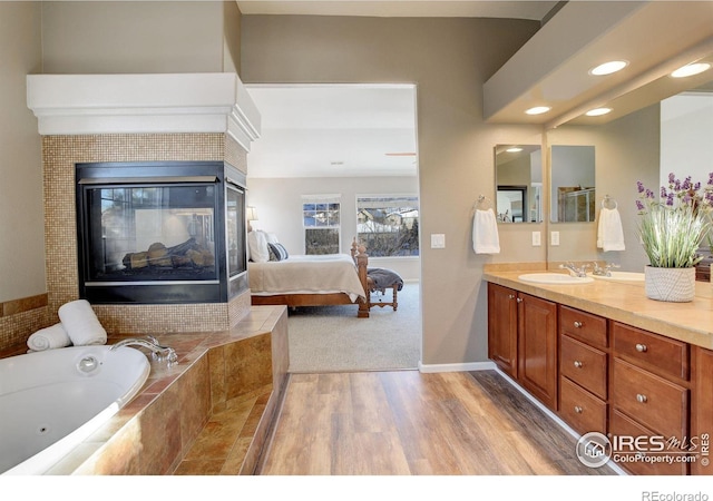 bathroom with a fireplace, hardwood / wood-style floors, tiled bath, and vanity