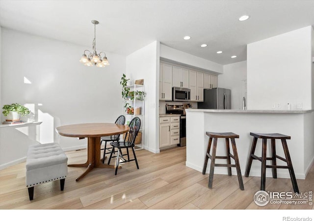 kitchen with hanging light fixtures, a kitchen breakfast bar, kitchen peninsula, stainless steel appliances, and white cabinets