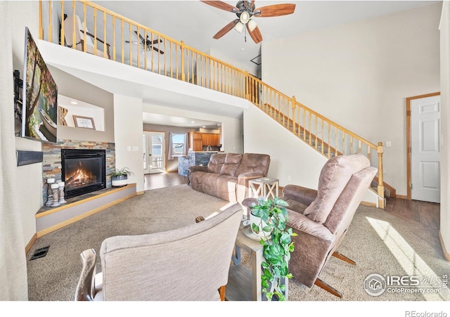 living room featuring a towering ceiling, ceiling fan, hardwood / wood-style flooring, and a stone fireplace