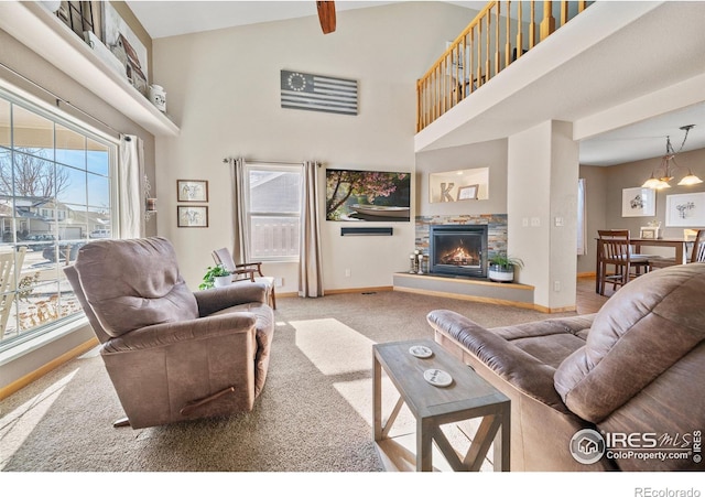 carpeted living room with high vaulted ceiling, a stone fireplace, and an inviting chandelier