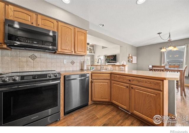 kitchen featuring appliances with stainless steel finishes, wood-type flooring, sink, kitchen peninsula, and backsplash