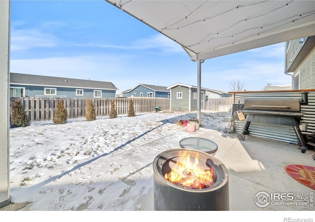 snow covered patio with an outdoor fire pit, a grill, and a shed