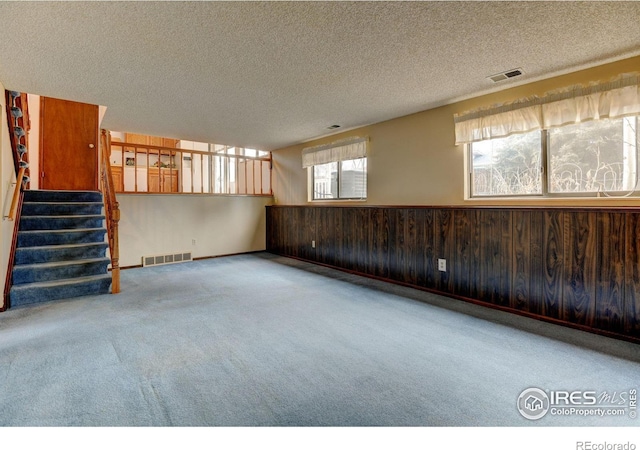 empty room with carpet floors, a textured ceiling, and wooden walls