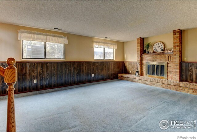 unfurnished living room featuring carpet, a brick fireplace, wooden walls, and a textured ceiling