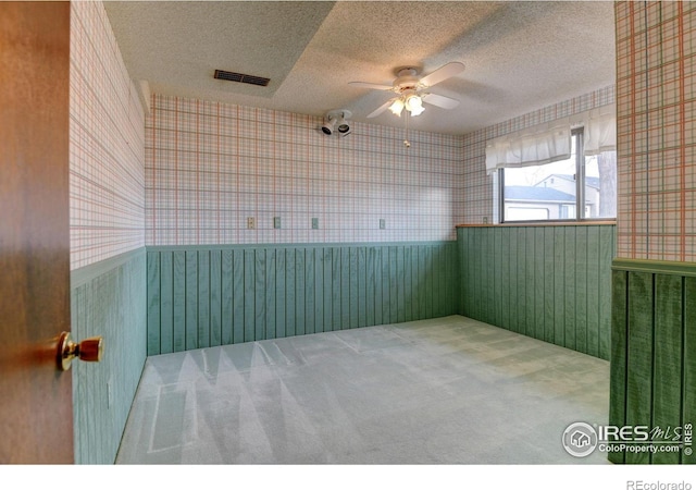 empty room featuring ceiling fan, a textured ceiling, carpet floors, and wooden walls