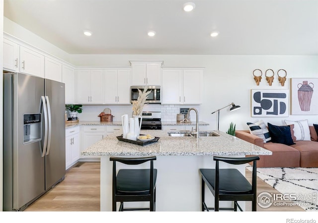 kitchen featuring appliances with stainless steel finishes, white cabinetry, a kitchen island with sink, sink, and a breakfast bar