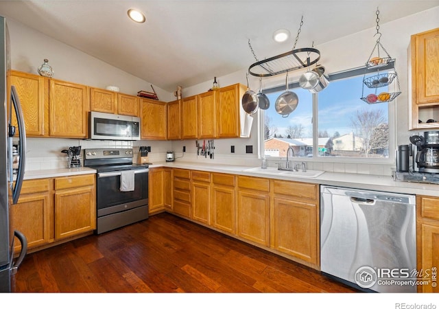 kitchen with appliances with stainless steel finishes, hanging light fixtures, sink, vaulted ceiling, and dark hardwood / wood-style floors