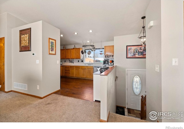 kitchen featuring kitchen peninsula, pendant lighting, dark carpet, sink, and an inviting chandelier