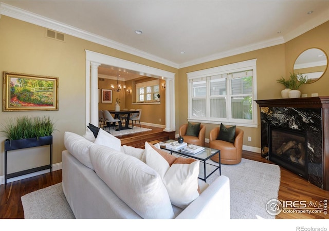 living room with crown molding, a fireplace, decorative columns, dark hardwood / wood-style floors, and an inviting chandelier