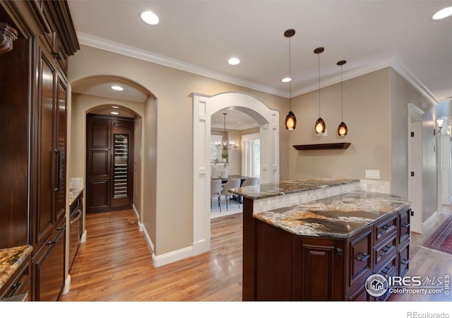 kitchen featuring pendant lighting, ornamental molding, dark brown cabinets, and dark stone countertops