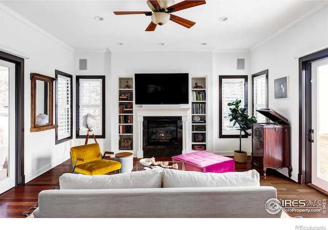 living room featuring built in features, dark hardwood / wood-style flooring, crown molding, and ceiling fan