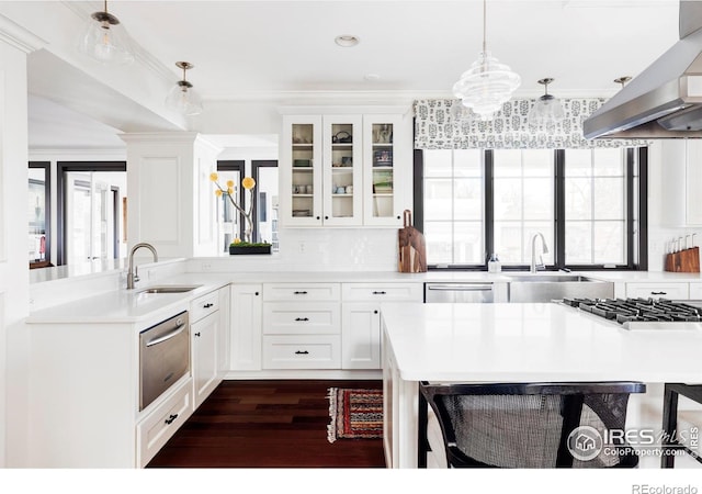 kitchen featuring pendant lighting, white cabinets, wall chimney range hood, sink, and crown molding