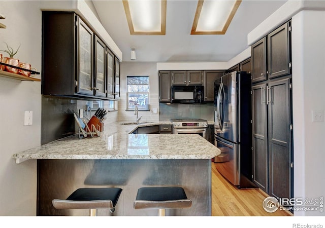 kitchen featuring stainless steel appliances, tasteful backsplash, light wood-style flooring, a sink, and a peninsula