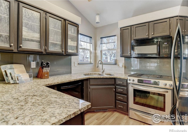 kitchen with lofted ceiling, dark brown cabinetry, backsplash, light stone countertops, and black appliances